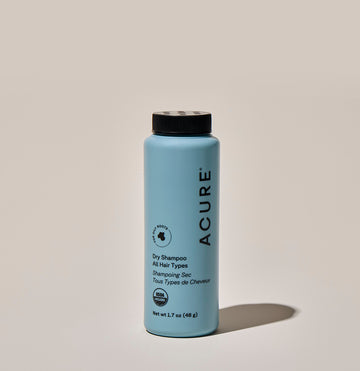 A bottle of ACURE dry shampoo on a neutral background.